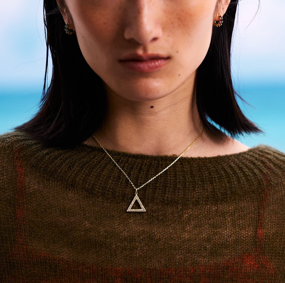 Close-up of a person wearing a gold triangle necklace with a blurred background