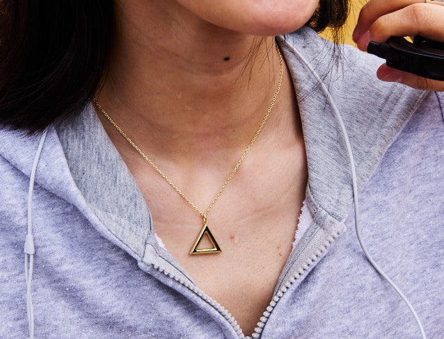 Person wearing a gold triangle necklace with a blurred background