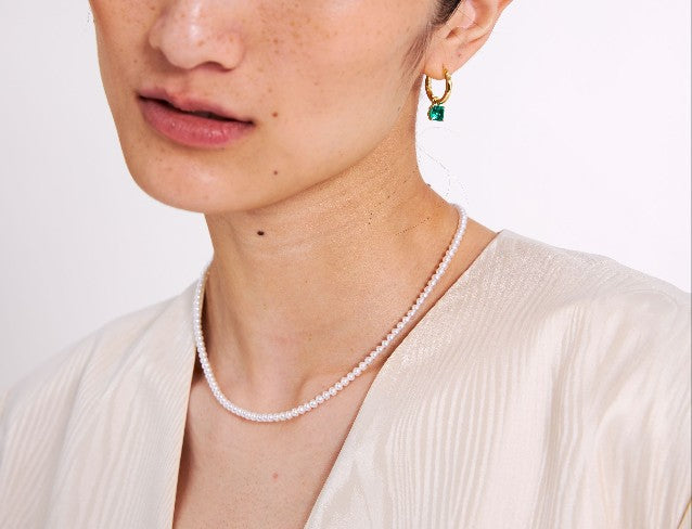 Close-up of a person wearing a pearl necklace and gold earrings with a white background