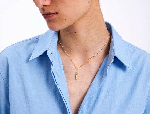 Person wearing a light blue shirt with a gold bar necklace