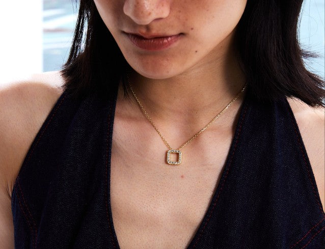 Close-up of a person wearing a gold necklace with a square pendant.