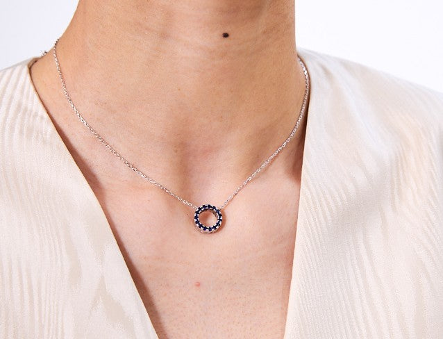 Silver necklace with a circular pendant worn by a person in a light-colored top.