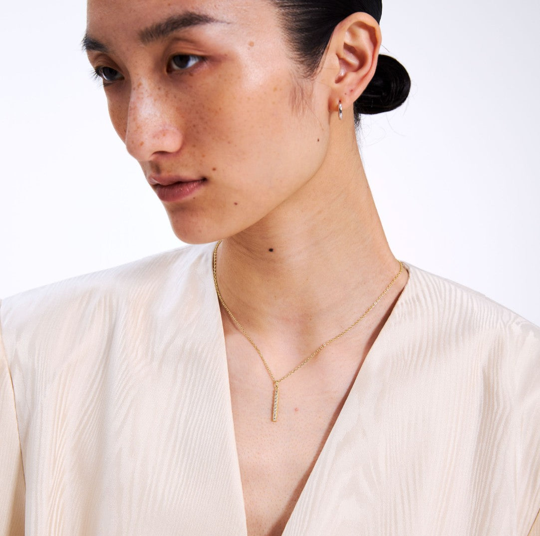 Close-up of a person wearing a gold bar necklace with a white background