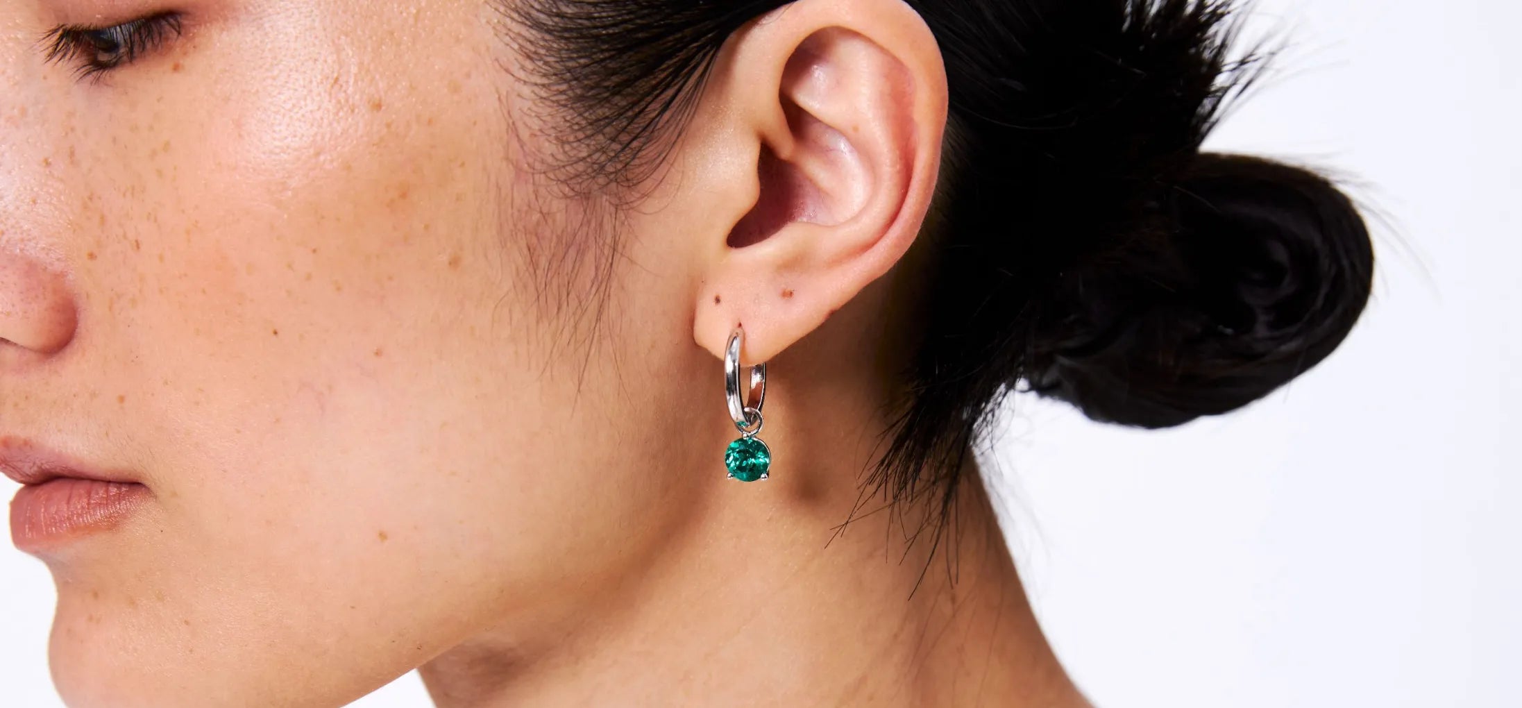 Close-up of a person wearing emerald green earrings with a white background