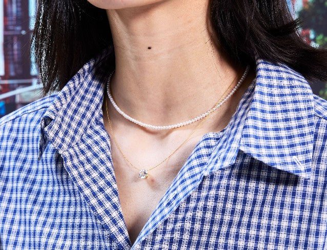Person wearing a blue and white checkered shirt with a gold necklace with white sapphire