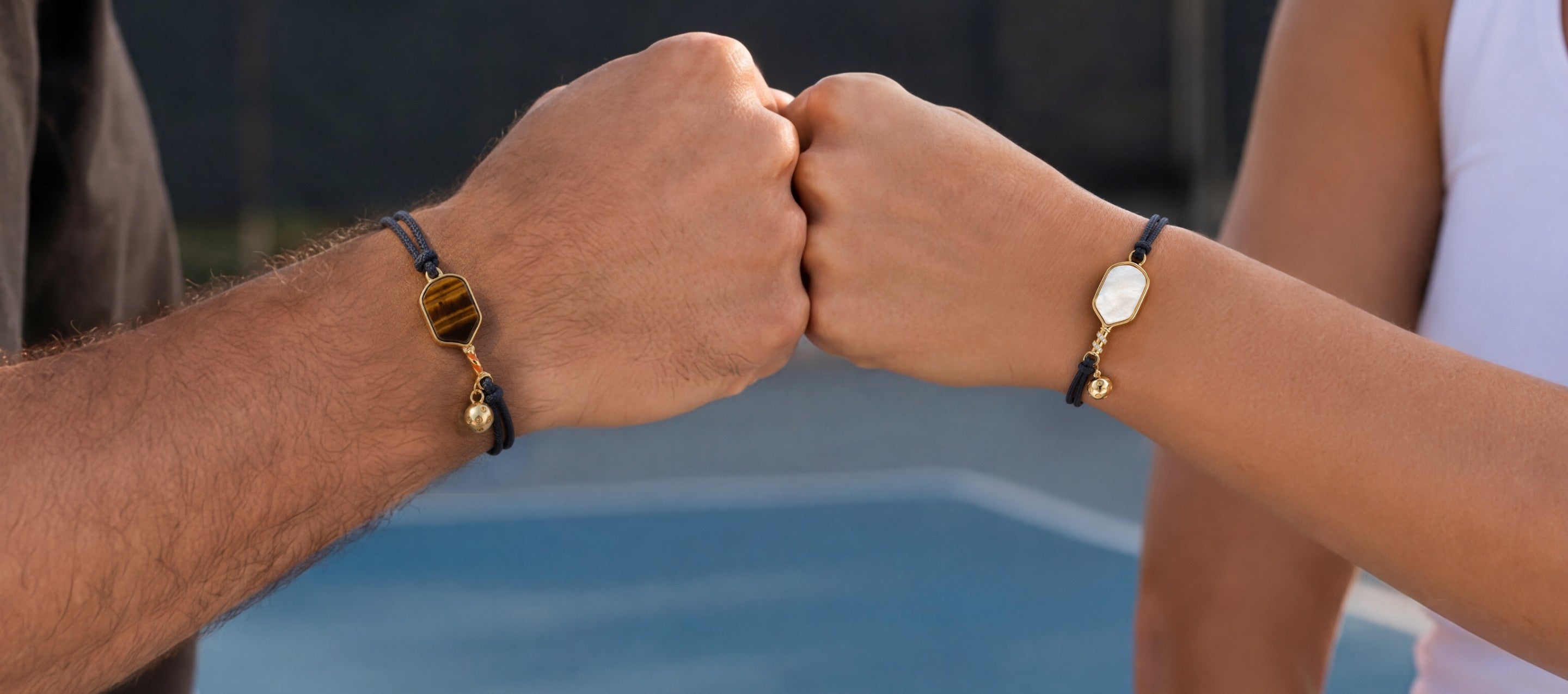 Two people holding hands with pickleball bracelets on, blurred background
