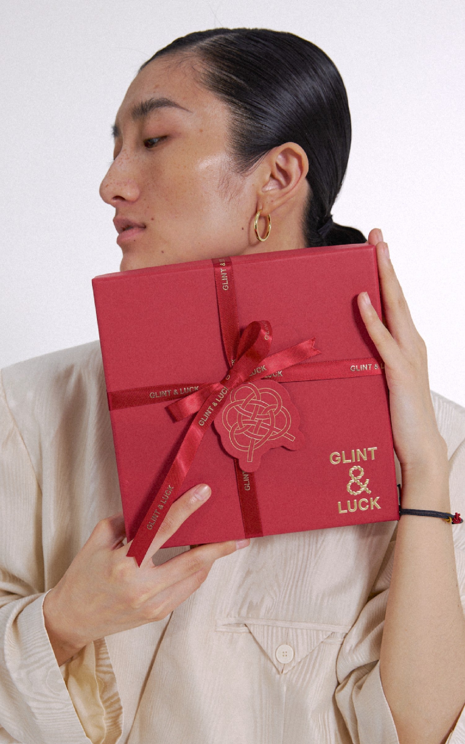 Person holding a red box with 'GLINT & LUCK' branding against a white background