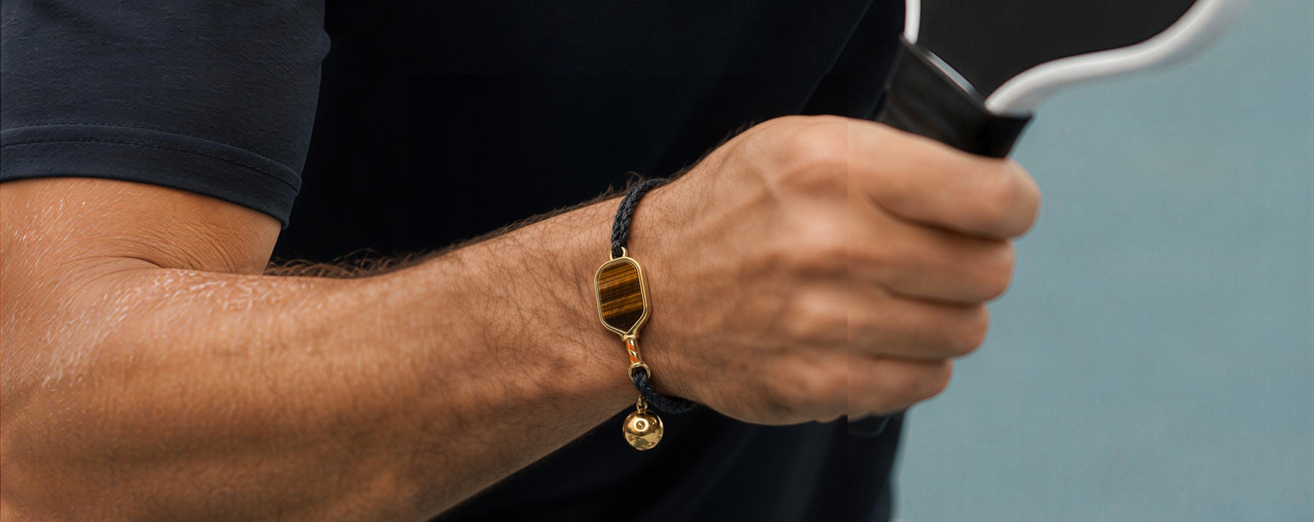 Person holding a tennis racket with a focus on a paddle charm pickleball bracelet.