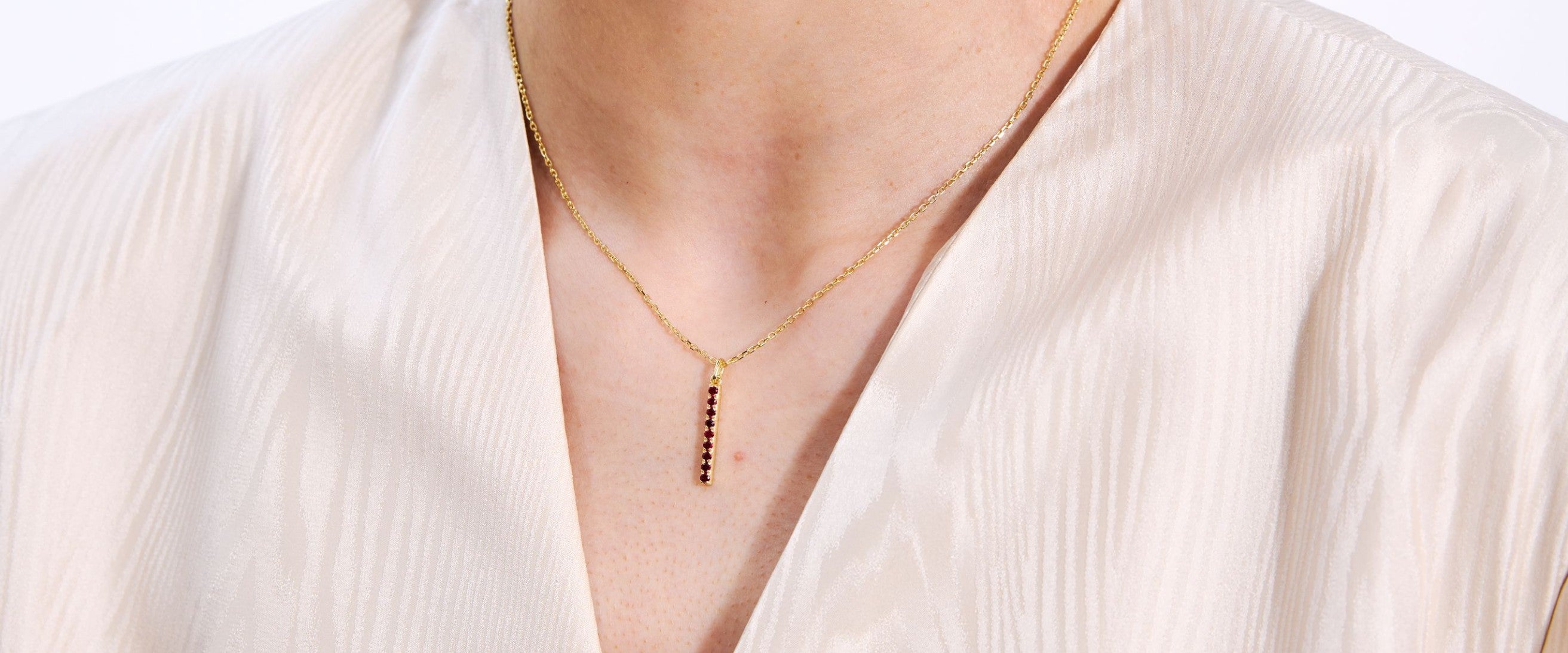 Gold bar necklace with red gemstones on a person wearing a white blouse.