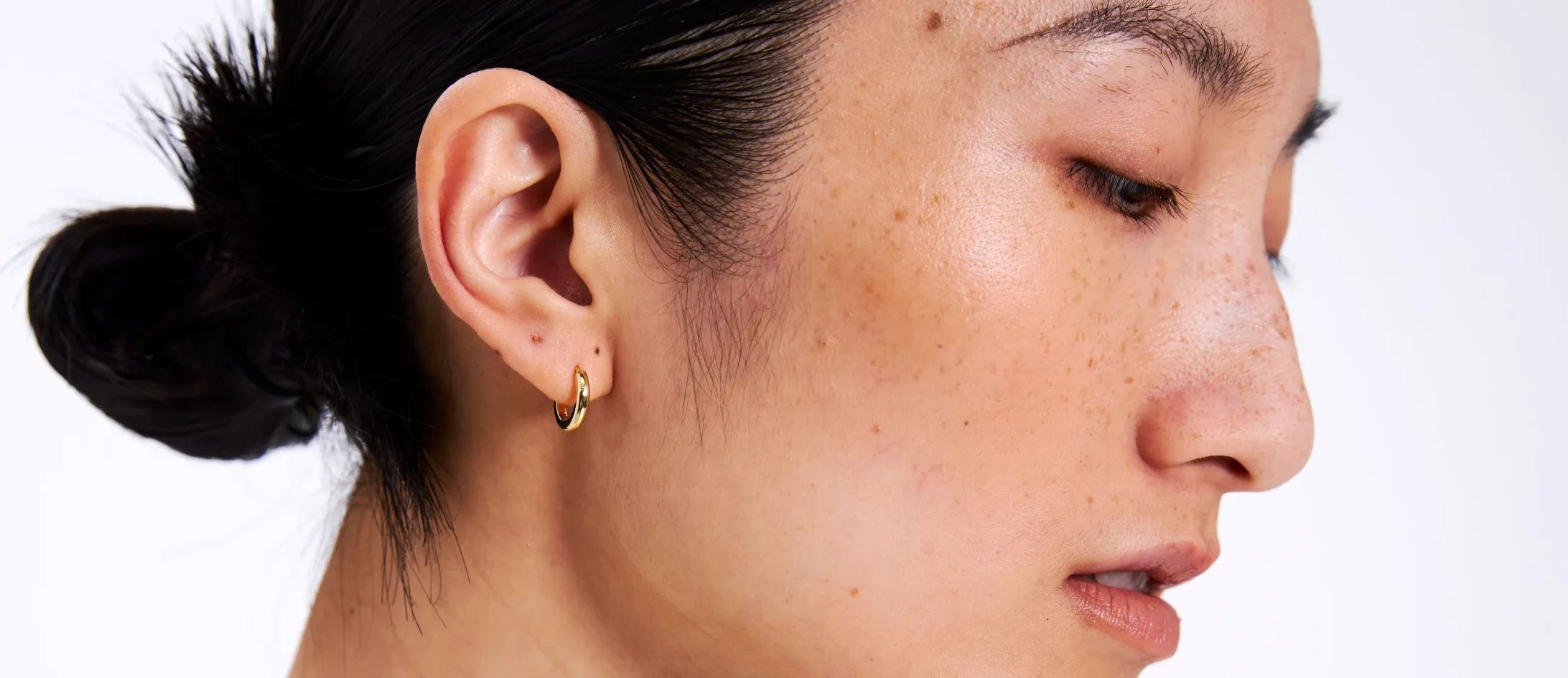 Close-up of a person wearing a gold earring on a white background