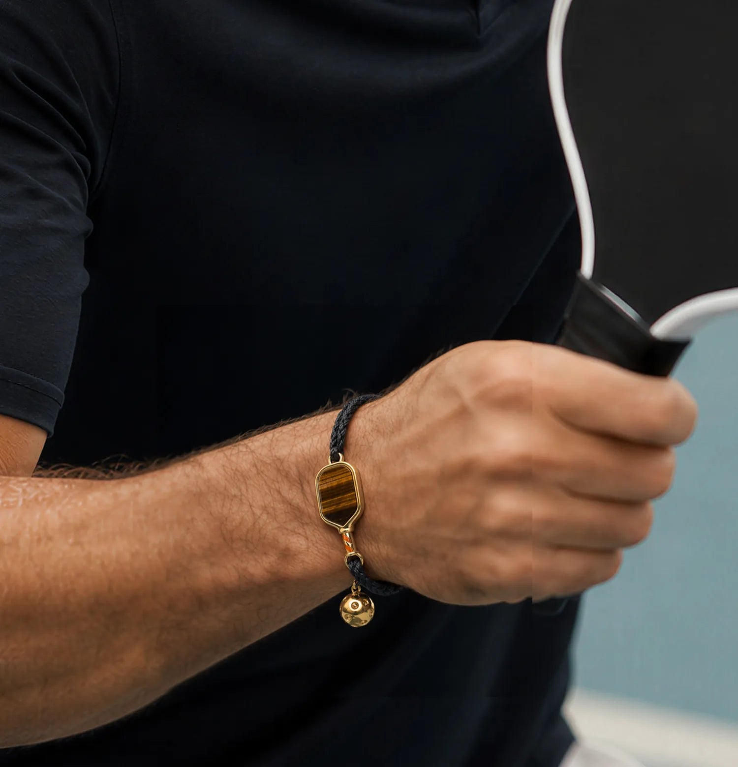 Person holding a paddle with a focus on a pickleball bracelet on their wrist.