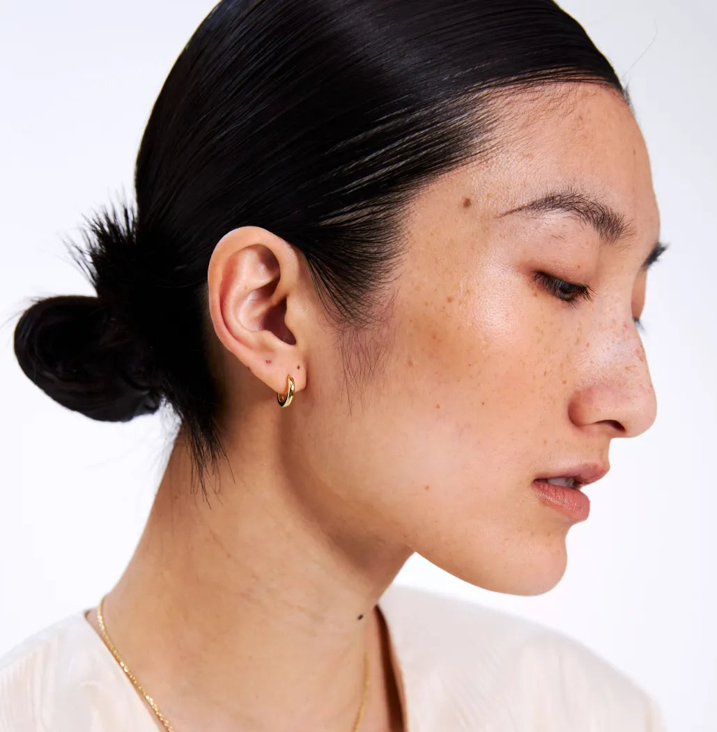 Close-up of a person wearing a small gold hoop with a neutral expression on a white background