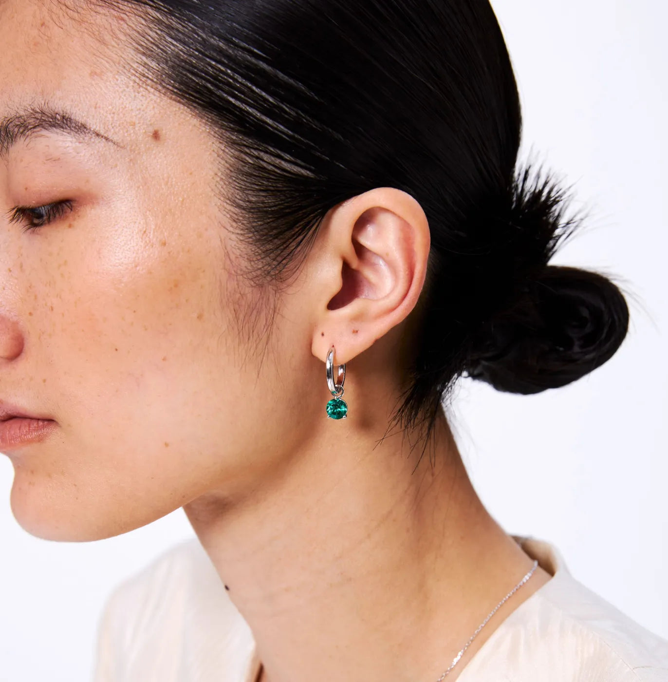 Close-up of a person wearing a silver hoop earring with a green gemstone on a white background